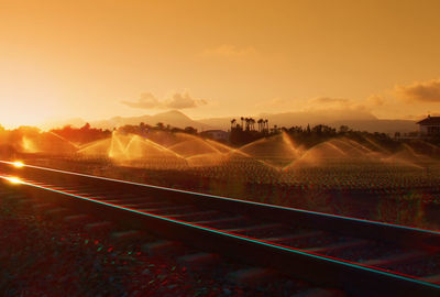 Railroad track by farm against orange sky