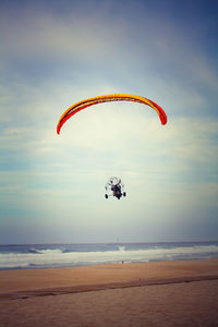Person paragliding over sea against sky