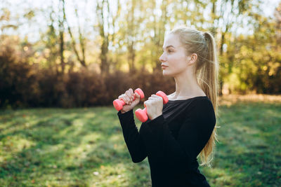 Profile of slim girl with dumbbells outdoors. fitness in park.