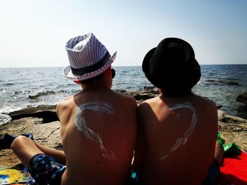 Rear view of friends sitting on beach against clear sky