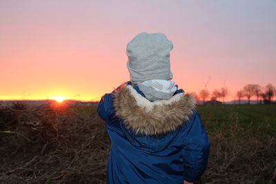 Rear view of woman standing on field against sky during sunset