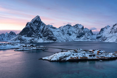 Scenic view of lake by snowcapped mountains against sky during sunset