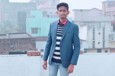 Portrait of young man wearing blazer standing on building terrace