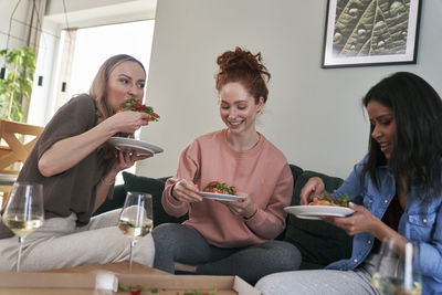 Cheerful female friends eating food at home