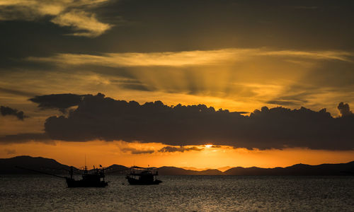 Silhouette boats in sea against dramatic sky during sunset