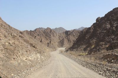 Dirt road leading towards mountains against clear sky