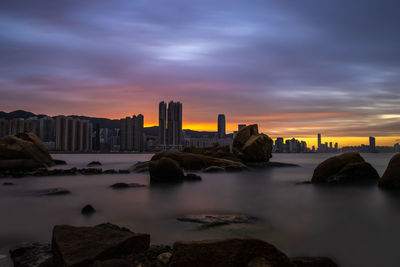 Sea by cityscape against sky during sunset