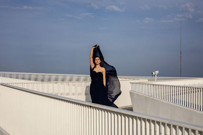 Woman standing on railing against sky