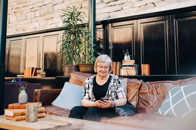 Senior female tourist using smart phone while sitting on sofa at restaurant
