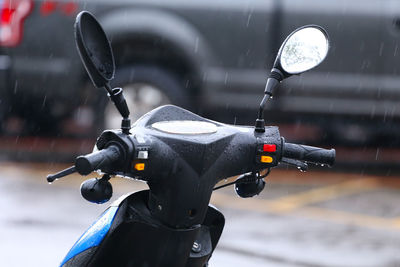 Close-up of motor scooter parked on road during rain