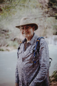Portrait of smiling man in hat standing against waterfall