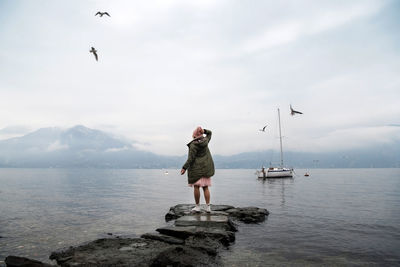 Full length of young woman standing in sea against sky