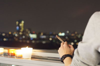 Cropped image of hand holding cigarette by illuminated candles at night