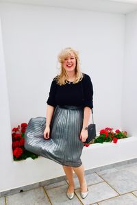 Full length portrait of smiling woman standing by wall