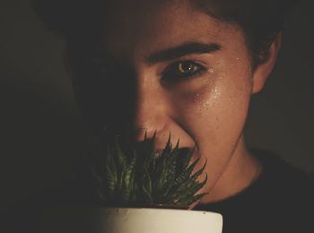 Close-up portrait of young woman with potted plant in darkroom