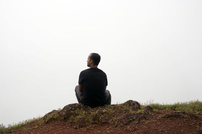 Rear view of man sitting on rock