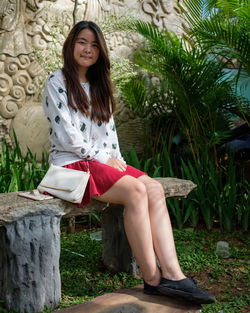 Portrait of smiling young woman sitting on bench in park