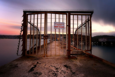 Metallic gate on pier over river during sunset