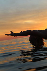 Silhouette person in sea against sky during sunset