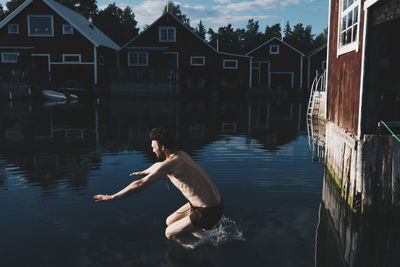 Side view of shirtless man diving in lake by chalets