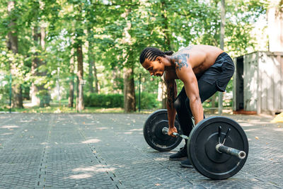 Shirtless young man holding barbell outdoors