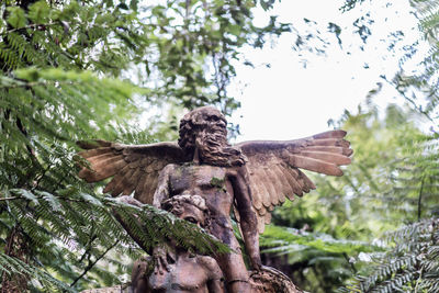 Low angle view of angel statue against trees