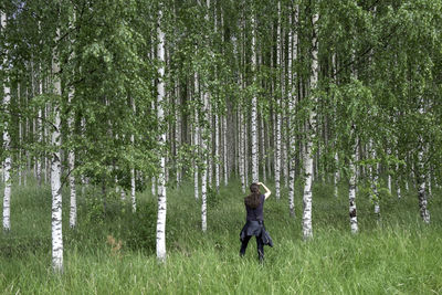 Woman standing by tree on field in forest