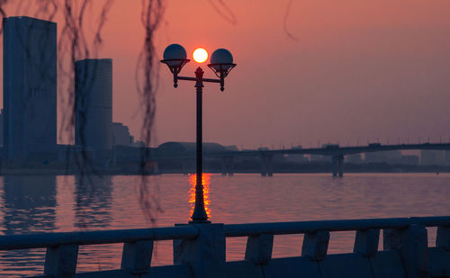 Street light by river against sky during sunset