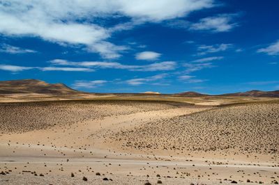 View of sand dunes in desert against cloudy sky