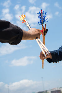 Low angle view of hands holding arrows against blue sky