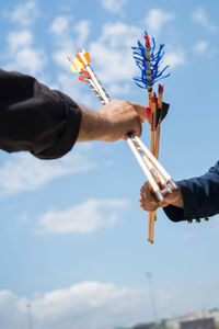 Cropped hands holding archery bow against sky