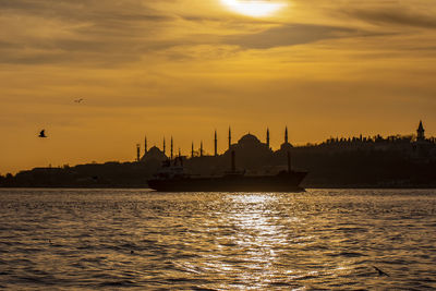 Silhouette mosques by sea against orange sky during sunset