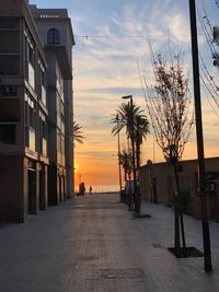 Footpath amidst buildings against sky during sunset