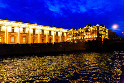 Illuminated buildings against blue sky at night