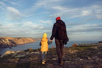 Rear view of man and boy standing on mountain against sky