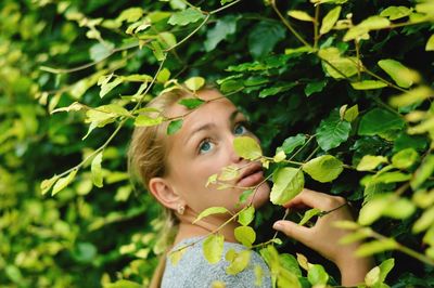 Close-up of young woman looking up while standing by plants at park