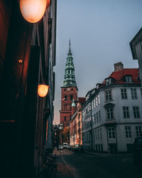 Illuminated street amidst buildings in city at dusk