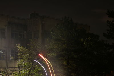 Light trails on street by buildings against sky at night