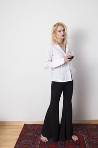 Full length portrait of woman standing by wall at home