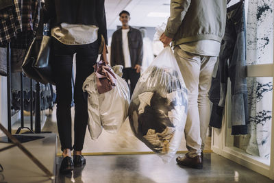 Low section of male and female fashion designers holding plastic bag of recycled clothes at workshop
