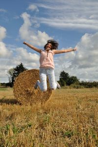 Full length of woman jumping by hay stack on field
