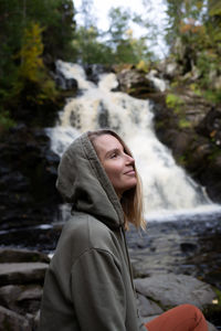 Portrait of young woman standing against waterfall