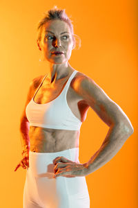 Portrait of young woman standing against yellow background