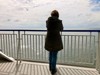 Rear view and silhouette of woman standing at the railing of a ship, gazing over the sea