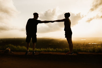 Silhouette couple fist bumping while standing on field against sky