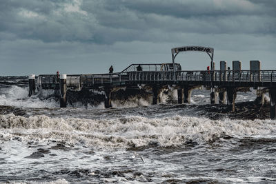 People on bridge over sea against sky