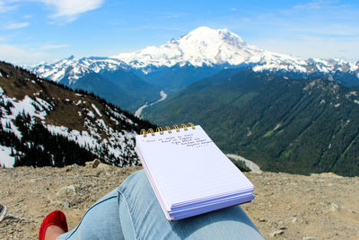 Person writing journal against mountains