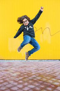 Full length of teenage boy jumping against yellow wall