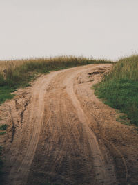 Dirt road amidst field against clear sky