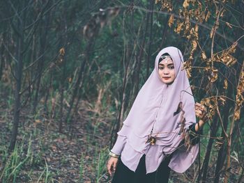 Portrait of young woman standing by tree in forest